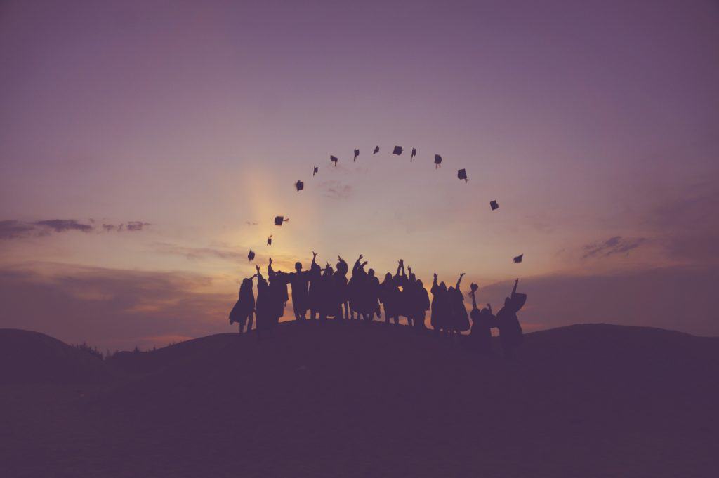 Image of Graduates tossing hats on hill during sunset