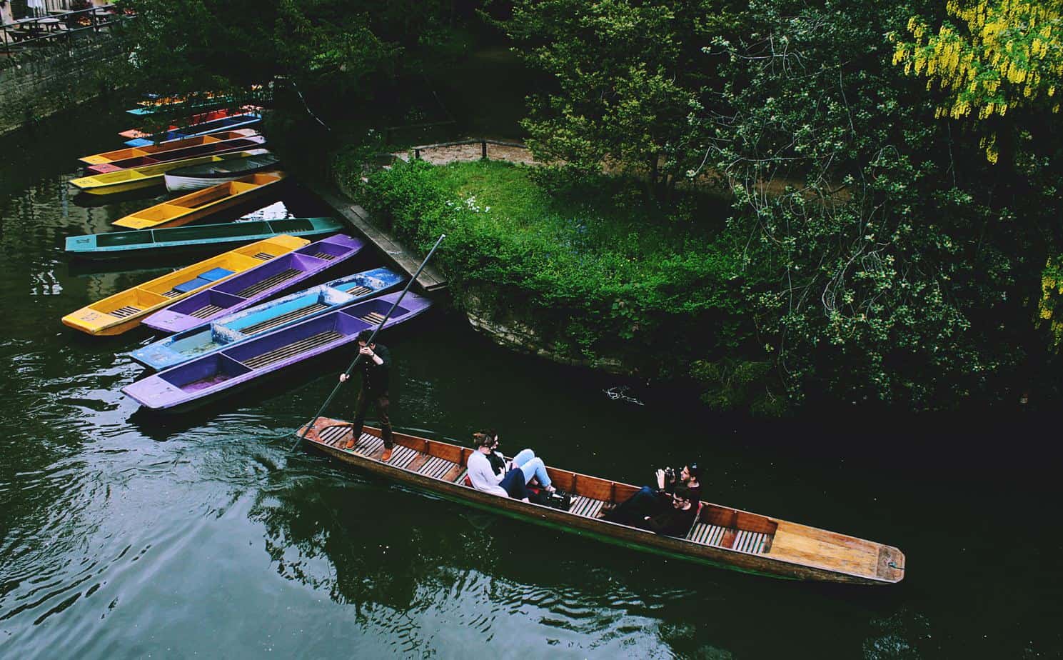 image of people punting on the river with colourful punts docked at the side of the river.
