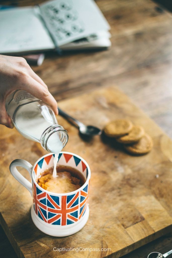 Britsish flag mug with tea. Milk being poured into cup and cookies (biscuits) in the background.