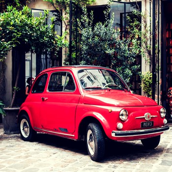 Image of old, red Italian car parked in cobblestone piazza