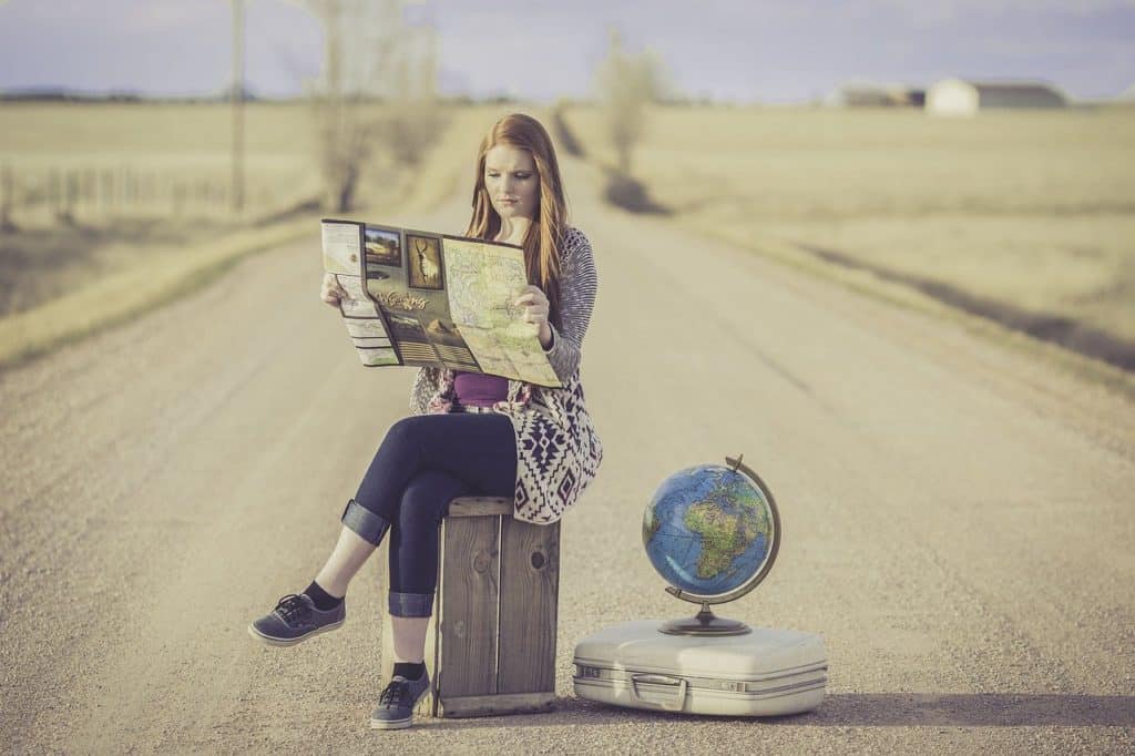 image of girls sitting on suitcase reading map with globe sitting next to her.